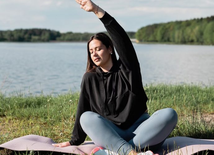 Woman enjoying a relaxing yoga session by a scenic lakeside. Perfect outdoor wellness setting.