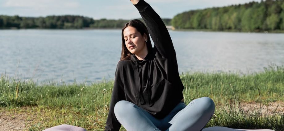 Woman enjoying a relaxing yoga session by a scenic lakeside. Perfect outdoor wellness setting.