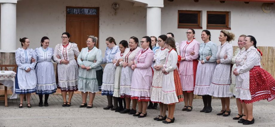 Women in colorful traditional folk dresses gather outdoors, showcasing cultural attire and community celebration.