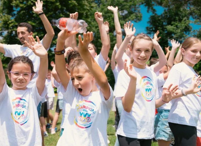 Group of cheerful children raising hands in a park during a sunny day, wearing t-shirts with event logos.